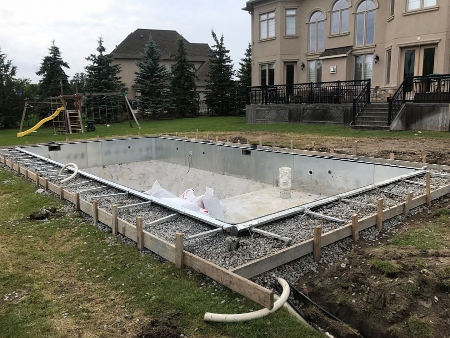 Gravel back-fill behind concrete frame for swimming pool installation.